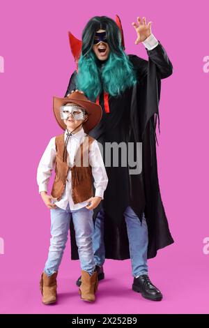 Happy father and son in costumes and carnival masks on purple background Stock Photo