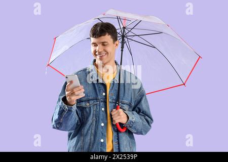 Young man with transparent umbrella using mobile phone on lilac background Stock Photo