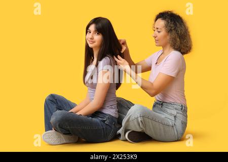 Beautiful mature woman brushing her teenage daughter's hair on yellow background. Mother's day Stock Photo