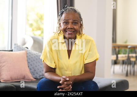 African American senior woman sitting at home, wearing a yellow shirt and jeans Stock Photo