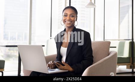 Happy African American professional woman in formal suit holding laptop Stock Photo