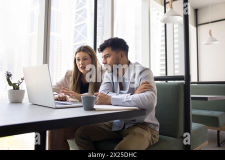 Serious male and female coworkers using laptop together Stock Photo