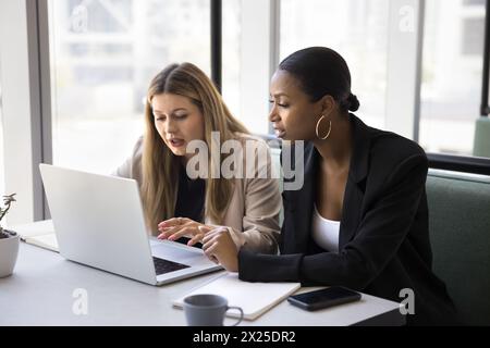 Two focused serious multiethnic female business colleagues discussing project Stock Photo