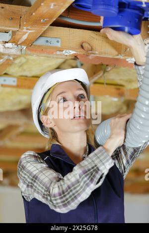 female electrician installing ventilation pipese in ceiling Stock Photo