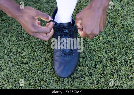 African American young male athlete tying black shoe laces on a grass field outdoors Stock Photo