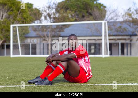 African American young male athlete sitting on soccer field outdoors, looking thoughtful Stock Photo