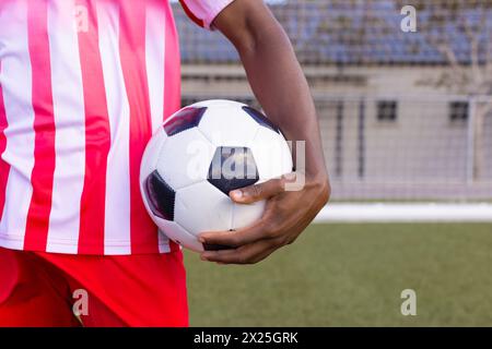 Black male athlete in red and white striped soccer gear holds a ball Stock Photo