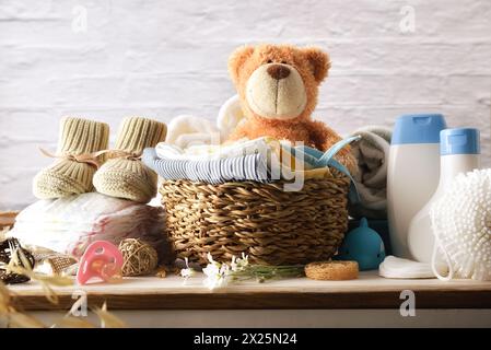 Clothes and accessories for clothing and baby grooming on wooden chest of drawers in room with white brick wall. Front view. Stock Photo