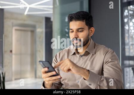 Focused young professional man browsing smartphone in a contemporary office setting. Captures a moment of modern work life with technology. Stock Photo