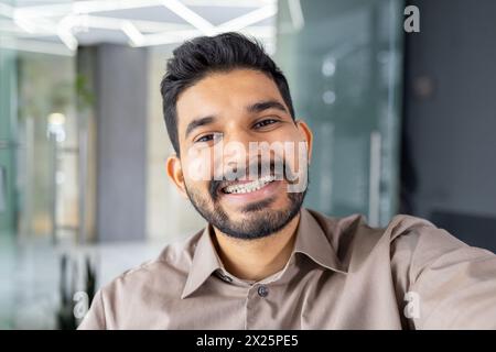 A beaming young man engages in a video call, showcasing warmth and friendliness as he looks directly into the camera, perhaps connecting with friends or family remotely. Stock Photo