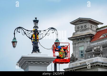 With the Fullerton Hotel in the background, electricians work on the lights over the historic 1910 built Anderson Bridge in Singapore's, civic area. Stock Photo