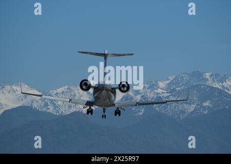 Airplane in flight against the backdrop of snow-capped mountains. The plane is preparing to land Stock Photo