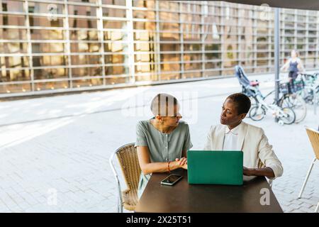 Two professional women engaging in a business discussion with a laptop at a cafe Stock Photo
