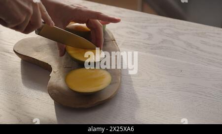 Man cutting ripe mango on olive board on white oak table, wide photo Stock Photo