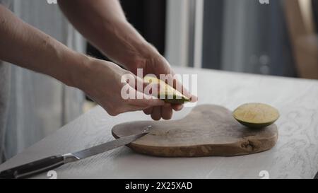 Man cutting ripe mango on olive board on white oak table, wide photo Stock Photo