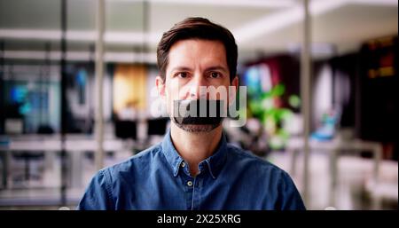 Young Man With Black Duct Tape Over His Mouth In Office Stock Photo