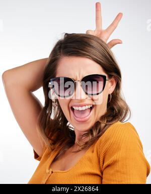 Stylish woman in bunny ears holding toy carrot and smiling on blue ...