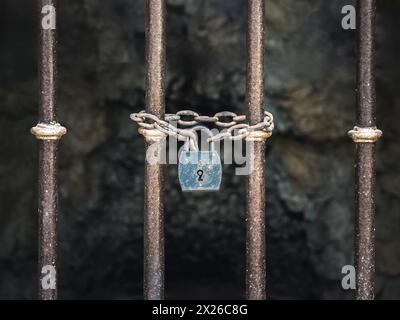 Vintage old rusty padlock with chains on an iron barred gate, dark background Stock Photo