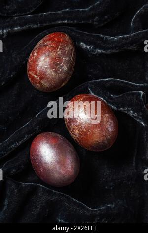 Eggs stained with wine and covered with mother-of-pearl on a dark velvet background. Easter concept, selective focus. Stock Photo