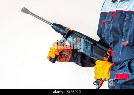 workman with a rotary hammer. Hands in protective gloves with hammer drill perforator. Copy space. Stock Photo