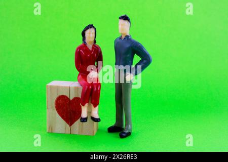 Woman sitting on wooden cubes that form heart and man standing next to her Stock Photo
