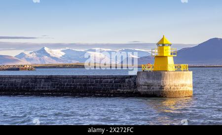 Panoramic view of a yellow lighthouse and harbour wall in Reykjavik at sunrise. Early morning with snow covered mountains in the distance. Iceland. Stock Photo
