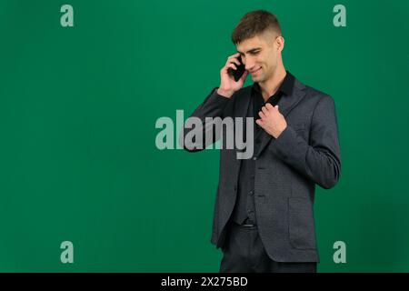 young bearded businessman or boss is seriously talking on the phone. emotions of a handsome man guy on a green background chromakey close-up dark hair young man. phone in hand gadget boss work ad Stock Photo