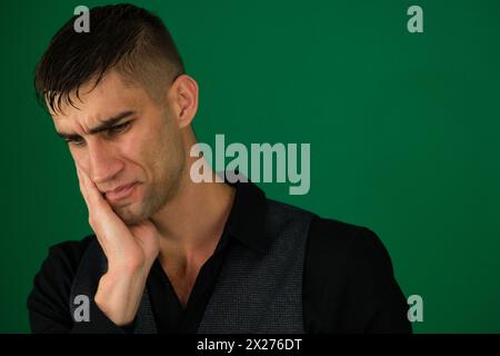 emotions of a handsome man guy on a green background chromakey close-up dark hair young man. Men Toothache Stock Photo