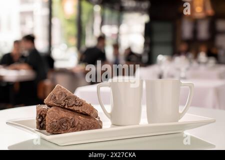 Three pieces of chocolate waffle cake with two cups on a white ceramic plate on the table, cafe background. Stock Photo