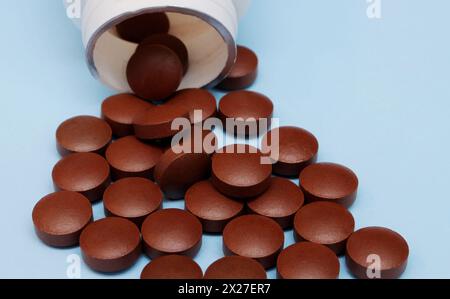 .Red round pills and bottles close up..Red-brown pills spilled out of a plastic bottle on a blue background close-up. Stock Photo