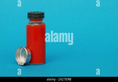 Glass medical bottle with a metal cap filled with blood. Bottle with red liquid on a blue paper background. Stock Photo