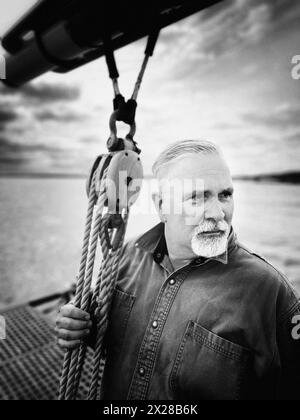 Head and shoulders portrait of mid-adult man looking away on sailboat Stock Photo