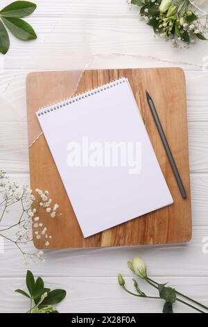 Guest list. Notebook, pencil, beautiful flowers and ribbon on white wooden background, flat lay Stock Photo