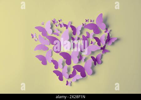 Heart made of violet paper butterflies on light yellow wall Stock Photo