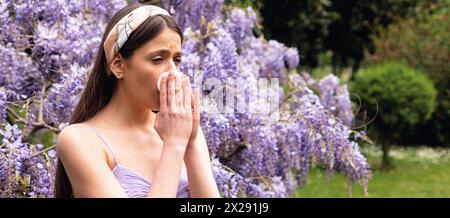 Spring allergy, flu. Banner. Girl with nose allergy sneezing. Polen illnes symptom concept. Woman allergic to blossom during spring blooming tree Stock Photo