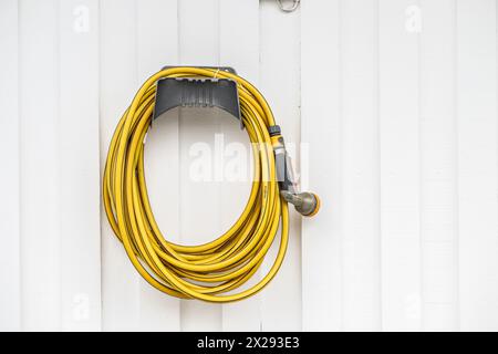 Yellow garden hose hanging on a house wall Stock Photo