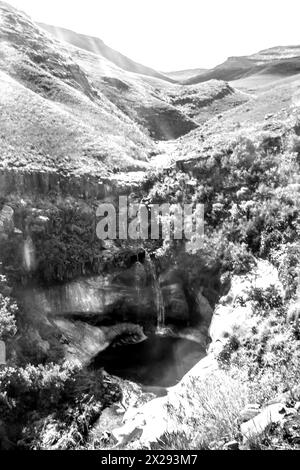 A small waterfall plummeting down to a deep secluded pool in the Drakensberg Mountains of Golden Gate National Park South Africa in Black and White Stock Photo