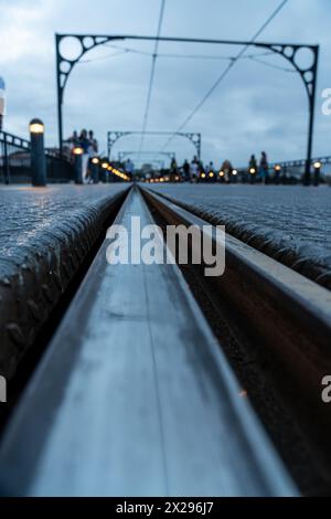 Porto metro train or tram track in infinite perspective at ground level of the Dom Luis bridge at sunset, under a cloudy sky and silhouettes of touris Stock Photo