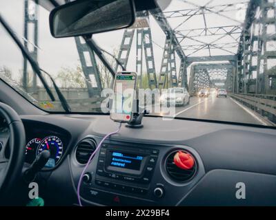 A car is driving on a bridge with a cell phone mounted on the dashboard. The phone is displaying a map and the car is surrounded by other cars Stock Photo
