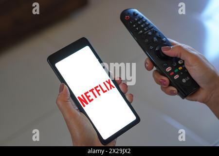 April 20, 2024, Brazil. In this photo illustration, the woman holds the TV remote control and the smartphone with the Netflix logo displayed on the sc Stock Photo