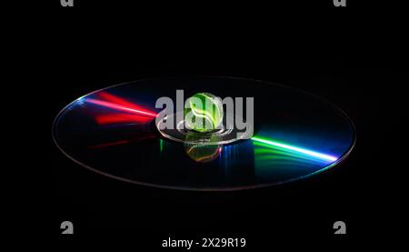 A green glass ball in the center of a CD with bright reflections on a dark background. Stock Photo
