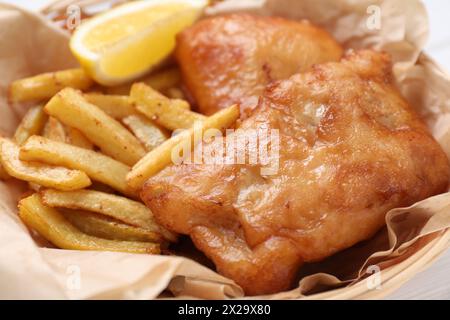 Tasty fish, chips and lemon in wicker bowl, closeup Stock Photo