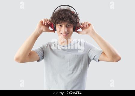Smiling and handsome, the young man wears headphones and is isolated against a gray background. He looks at the camera with his blue eyes while listen Stock Photo