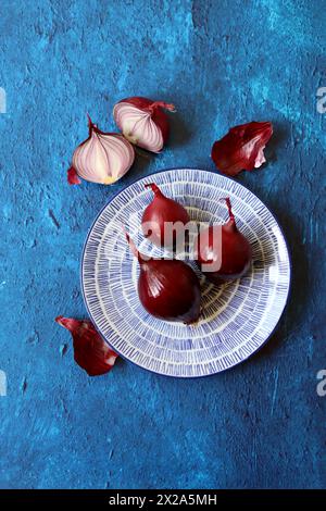 Red onion on a blue plate. Close up photo of fresh vegetables. Still life with onion on textured vibrant blue background with copy space. Stock Photo