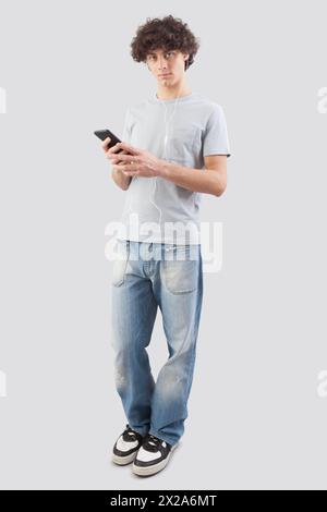 Young man, smiling and handsome, using his smartphone with earphones to listen to music or a voice message. He looking into the camera with his blue e Stock Photo