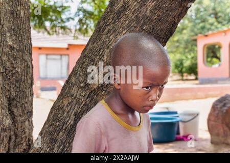 abused upset village african child, hiding behind a tree, standing in front of the house, Stock Photo