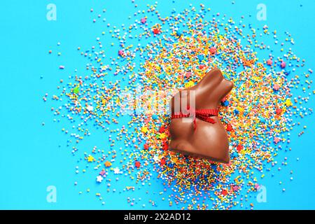 Chocolate bunny and colored sugar sprinkles on a blue background, top view. Easter composition. Easter chocolate bunny. Festive sweet treat. Chocolate Stock Photo