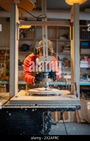 Man carpenter in noise-cancelling headphone, respirator working on drilling cnc machines in joinery Stock Photo