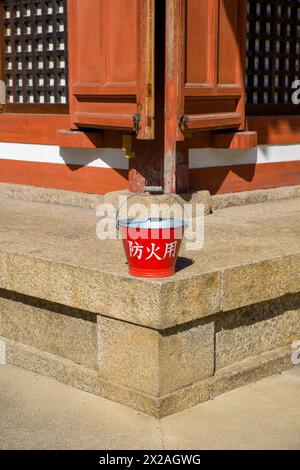 a red bucket with the japanese inscription 'for fire protection' in front of an old wooden building Stock Photo