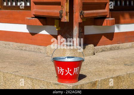 a red bucket with the japanese inscription 'for fire protection' in front of an old wooden building Stock Photo